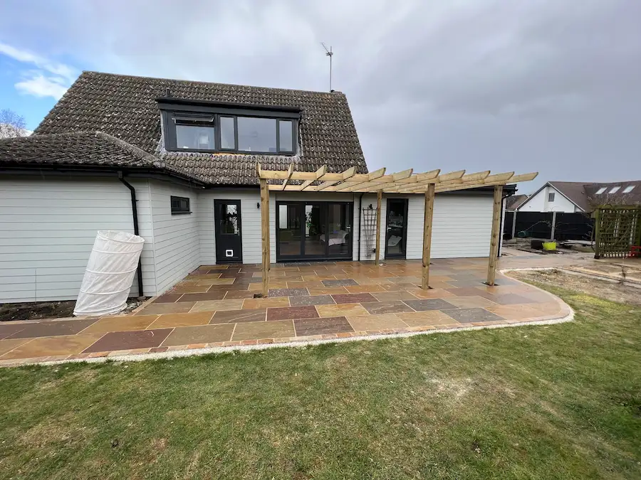 Brown and grey stone patio for house, with unfinished pergola